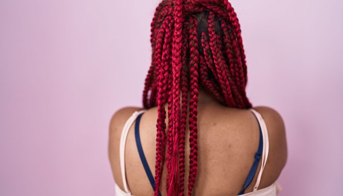 African american woman with braided hair standing over pink background standing backwards looking away with crossed arms