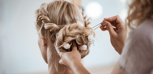 Female hairdresser making hairstyle to beautiful blonde girl in beauty salon. Copy space.